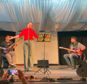Caty & The Morrones: la fuerza de la tierra hecha canciones Por Rosana Zeballos En el marco de la muestra “Campo Grande Expone”, una banda emergente del Paraje El Arroyón brindó un show que atravesó al público con la energía de los verdaderos artistas. Es sábado a la noche y en la sala Hugo del Carril, de Cinco Saltos, no cabe ni un alfiler. Los asistentes coparon las sillas y se acomodaron en los pasillos, sentados en el piso, y parados al fondo. Es la primera vez que este espacio logra este récord de asistencia, así que la organización tiene en sus ojos una mezcla de sorpresa y alegría. Contra todo pronóstico, quienes han logrado lo que nadie son artistas emergentes: una muestra de pinturas de una localidad vecina y la banda Caty y los Morrones, del Arroyón. Esta banda hace hoy su debut oficial, sin embargo, ya cuenta con muchas presentaciones amateurs. Hay un público que espera a su estrella desde temprano, se saludan entre abrazos, se acomodan en grupos y sonríen emocionados al ver a sus integrantes caminar por la sala. Pero también hay muchos otros que vinieron sin conocerla, y que están a punto de descubrir un show impactante. Música para mis oídos, café para mi alma Las luces se apagan. La muestra de arte ha terminado, empieza el show. Caty, la líder y vocalista de la banda ingresa a la sala con un cuenco entre las manos. Sahuma la sala y toda la atmósfera se llena de un aroma delicado, conocido. En el escenario, en simultáneo, empiezan a sonar los primeros acordes, mientras ella danza etérea, entre la gente. Una vez arriba, Caty toma el micrófono y se presenta como una artista rural, la enorgullecen sus orígenes, pronuncia con fuerza el nombre del Arroyón. Ese paraje, tantas veces infravalorado, tiene en ese momento la frente en alto. Inicia el repertorio y las bocas de los presentes empiezan a moverse entonando esos “clásicos que sabemos todos”. El blues, el funky y el rock se apoderan de la sala interpretados maravillosamente por esta artista, dueña de una voz privilegiada. Es imposible no entrar en la magia, la masa de gente se deja transformar por la melodía. Mientras la música suena, un grupo de amigas reparten entre el público pequeños vasitos de un caliente y delicioso “café de higo”. El show ha completado su círculo. Los asistentes recibieron su cuota de placer, y pueden volver a casa con los cinco sentidos satisfechos. Cuando la presentación finaliza (luego de varios bises) la gente sale despacio, como sin ganas de volver a la realidad. Más abrazos, felicitaciones, las miradas con el brillo de la emoción. Caty se funde entre su gente, vuelve a ser la madre, la amiga, la mujer que cada día cocina con productos de su huerta. Lo ha mostrado en una noche de música, pudo fusionar ese amor por la tierra con su pasión por la música. Los músicos bajan como quien ha ganado una batalla. Terminó la primera presentación, ahora están seguros de que no será la última. Ya no hay marcha atrás: el arte rural entró por la puerta grande, y ganó esta noche, su lugar.